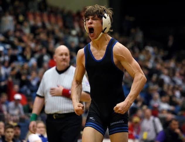 A wrestler roars in celebration in front of a packed state-tournament crowd