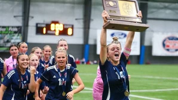 A girls soccer team lifts a state trophy together